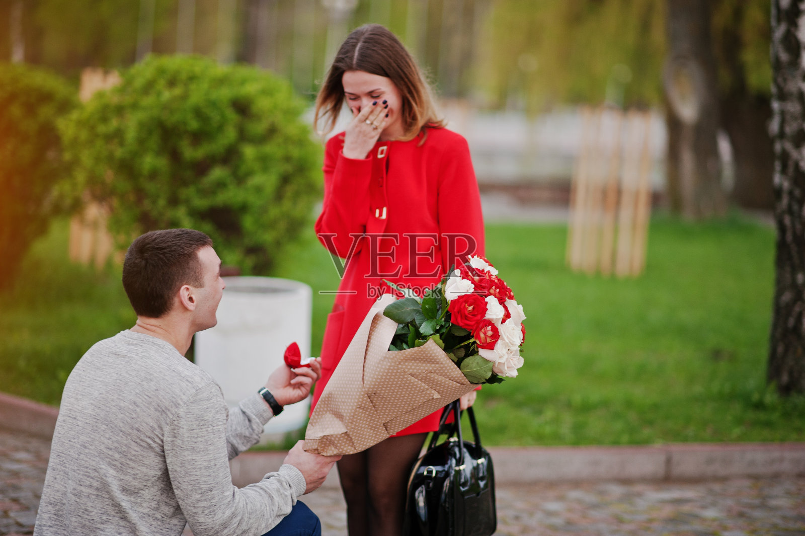 求婚。一个男人带着鲜花跪着，给他的女朋友送订婚戒指照片摄影图片