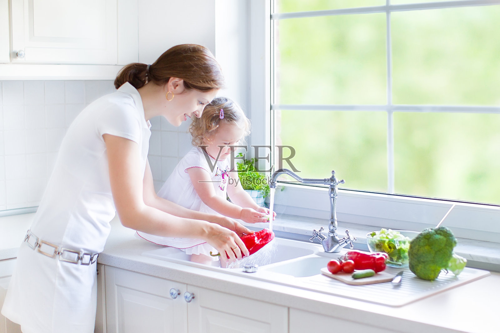 美丽的母亲和她的女儿在厨房的水槽里洗蔬菜照片摄影图片