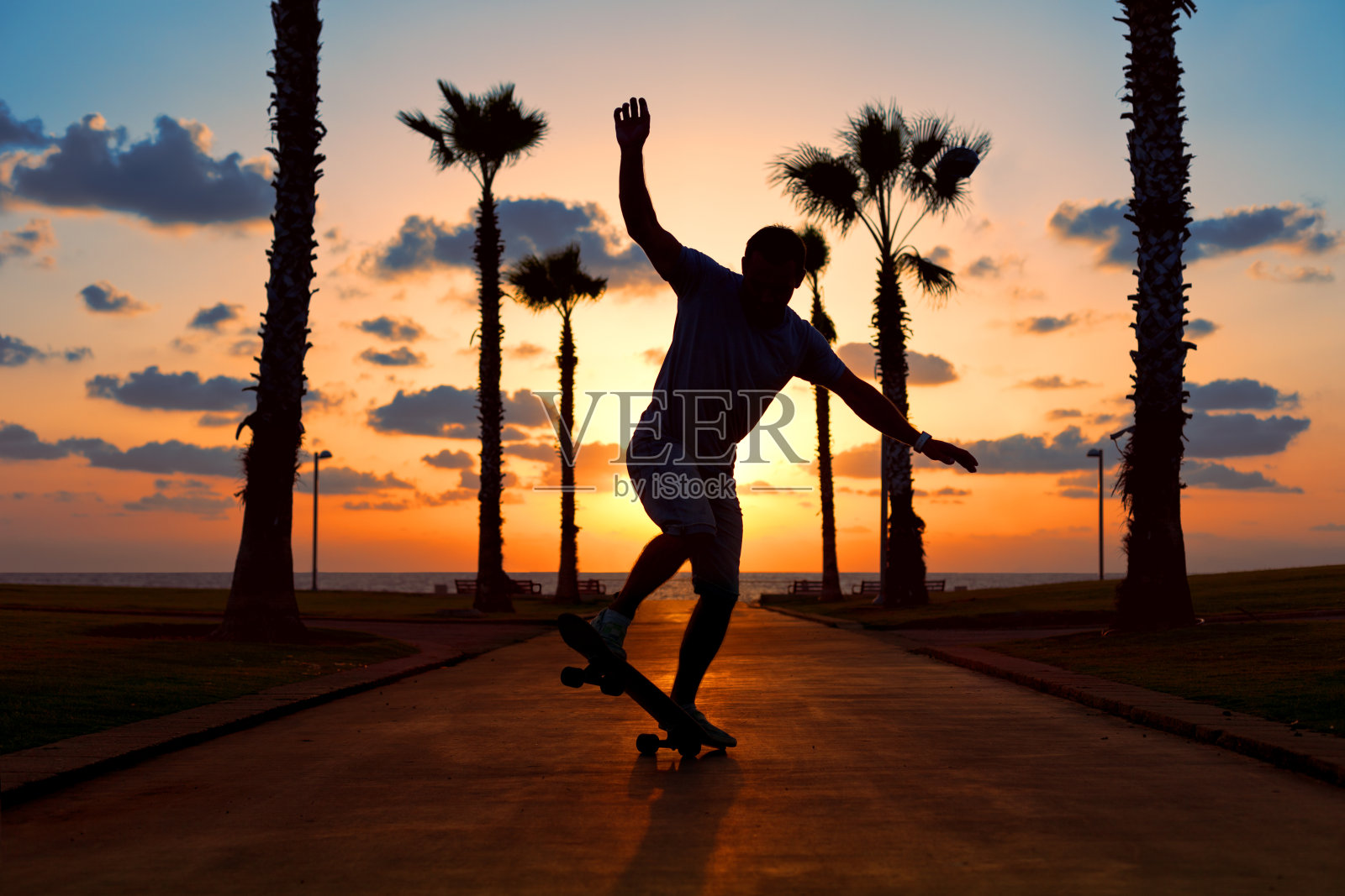 日落时分，一名男子在海边玩滑板照片摄影图片