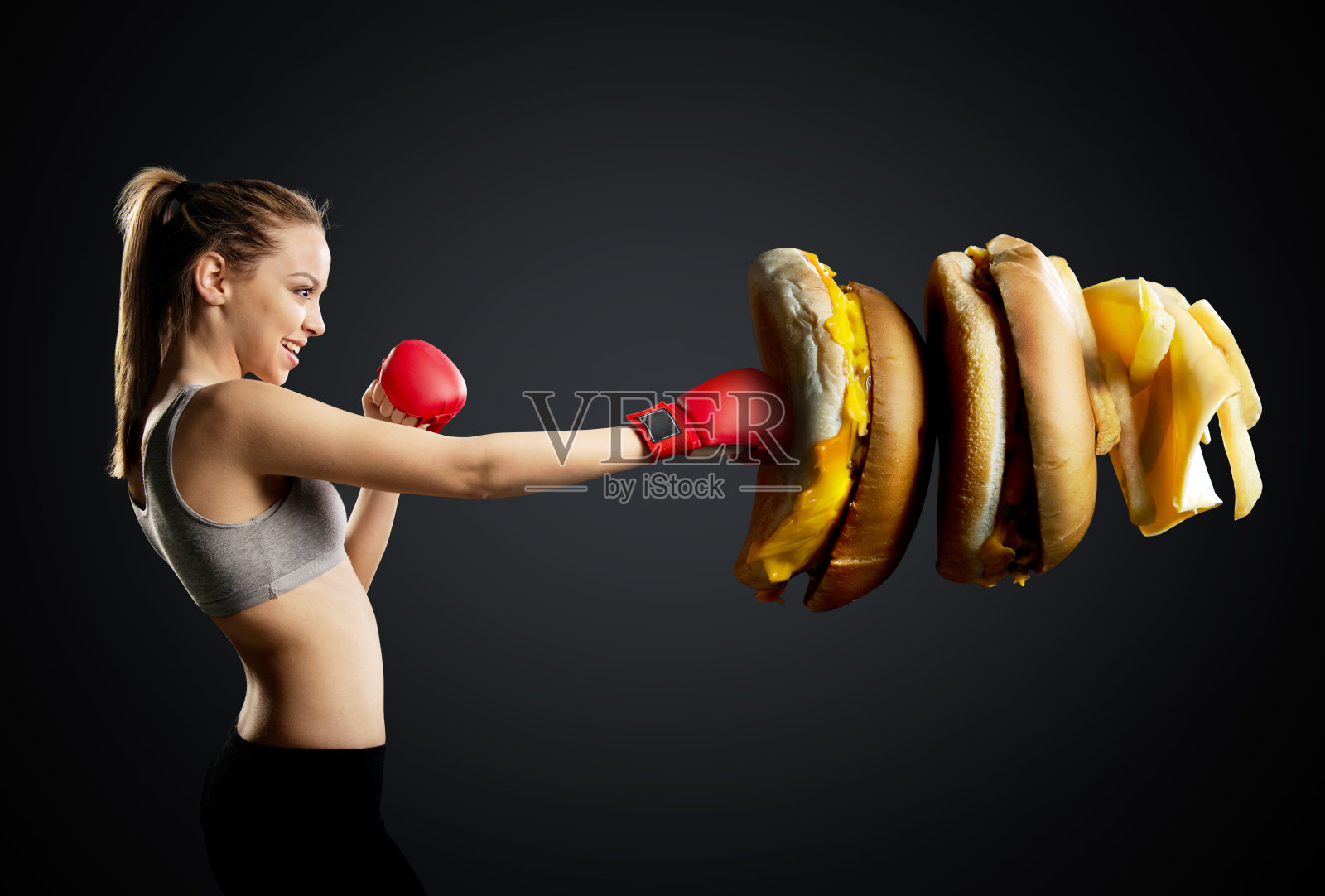健康，年轻，精力充沛的女人拳击不健康的食物，黑色背景照片摄影图片