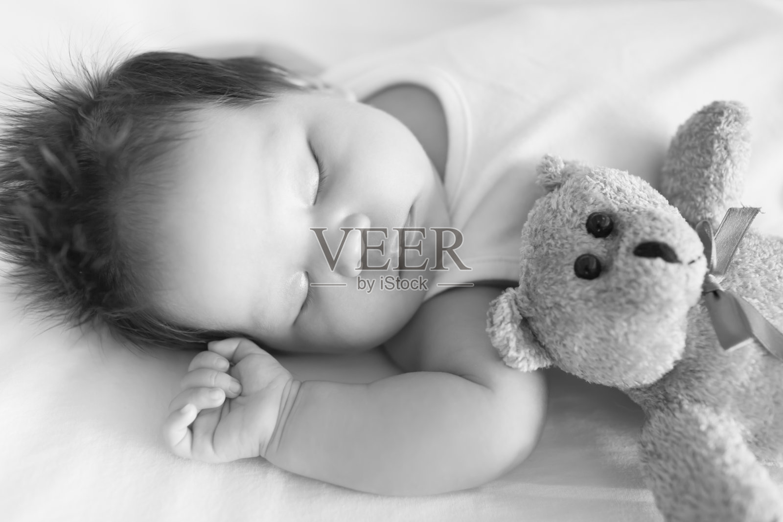 可爱的婴儿，安静地睡在婴儿床旁边的泰迪熊在一个凉爽的下午黑白。照片摄影图片