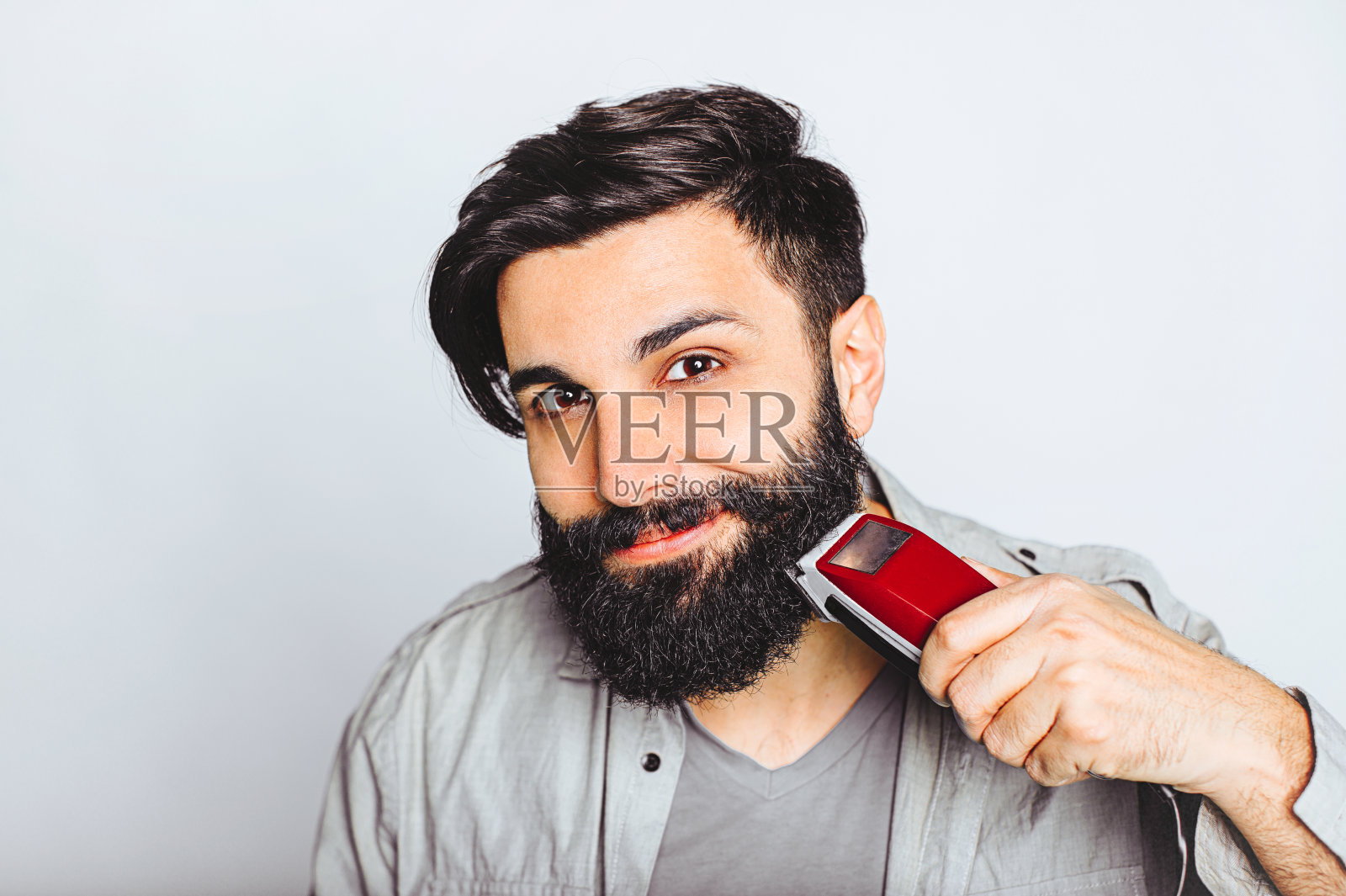 年轻的大胡子男子与电动剃须刀摆姿势照片摄影图片