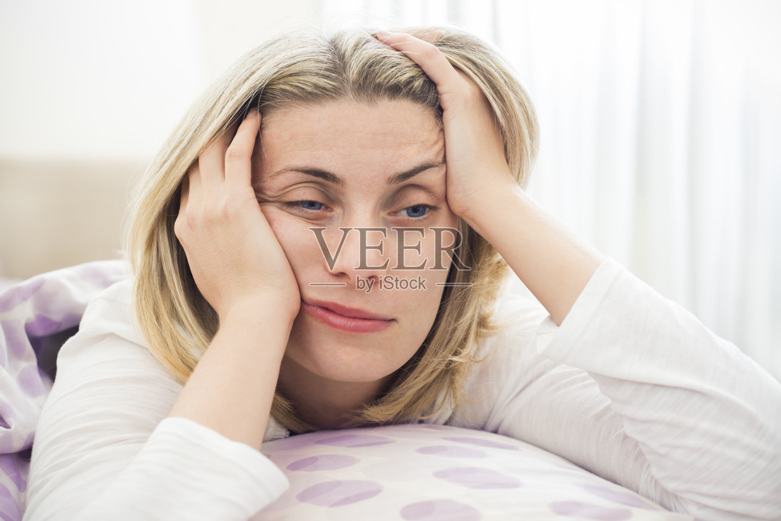 一个金发女人，双手托着头，躺在床上照片摄影图片