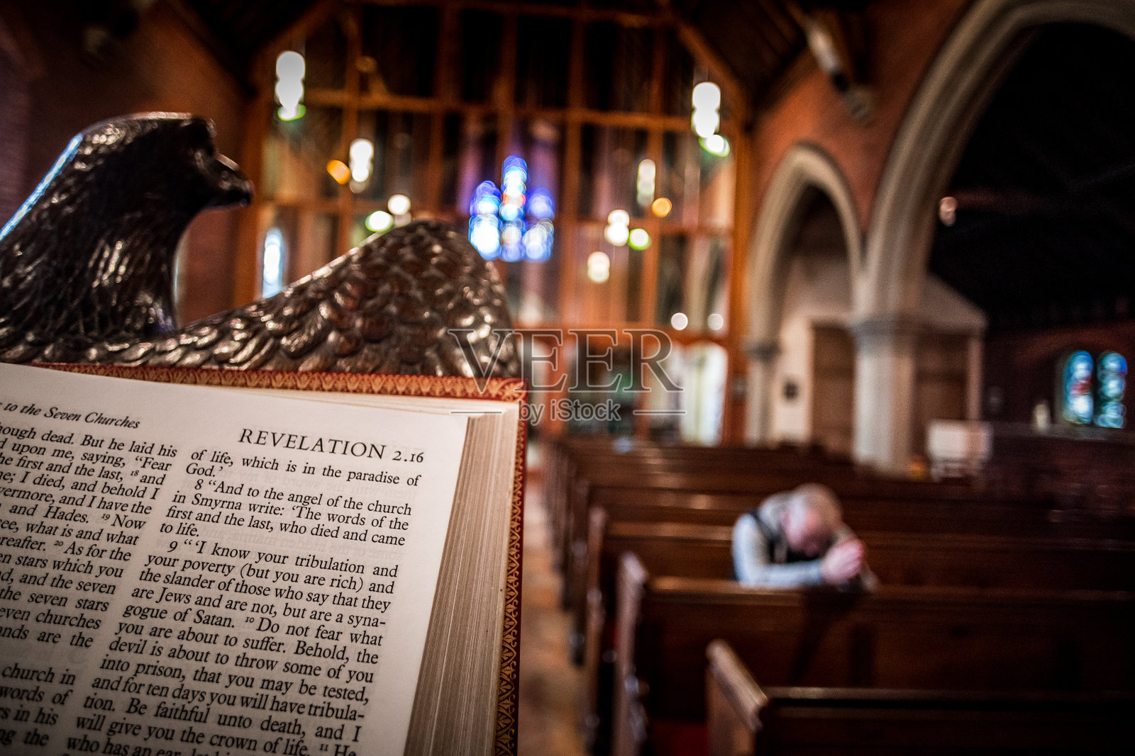 一名男子在英国国教教堂内的长凳上祈祷，焦点放在前景中的圣经上照片摄影图片