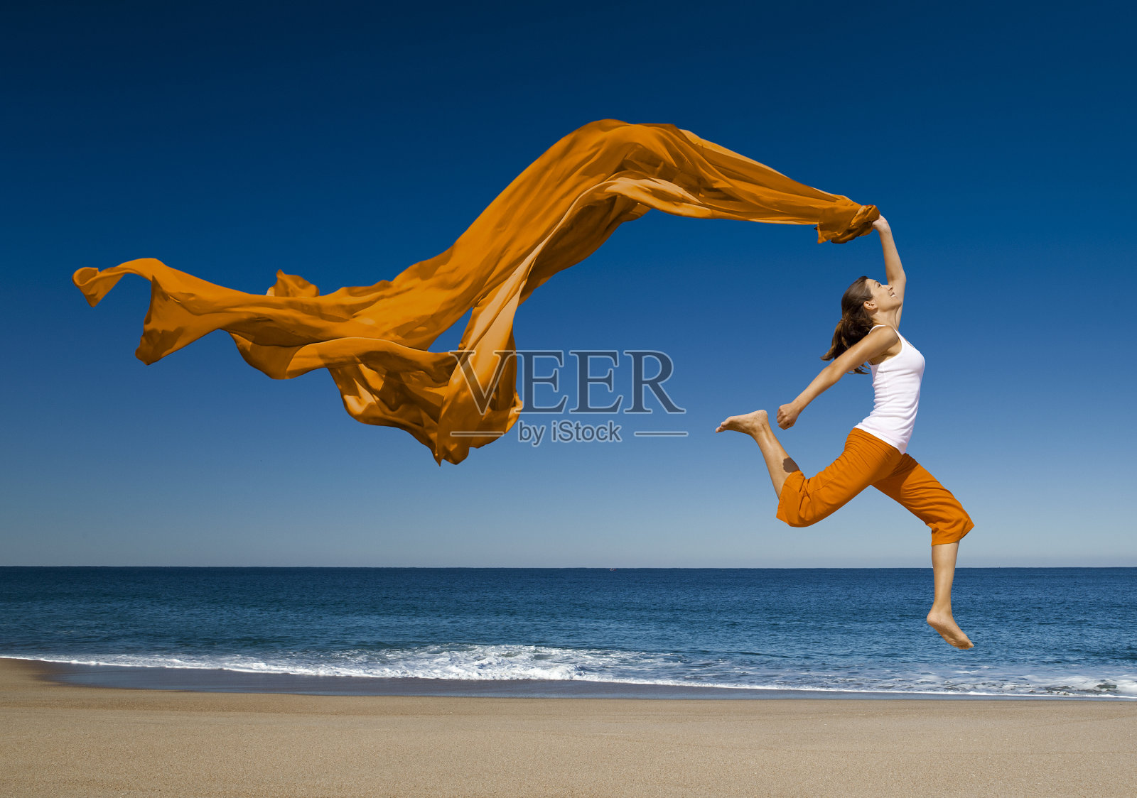 戴着橙色围巾的女人在海滩上蹦蹦跳跳照片摄影图片