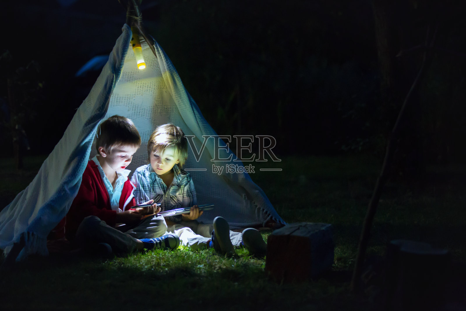 可爱的小弟弟们，晚上在帐篷里玩平板电脑和电话照片摄影图片