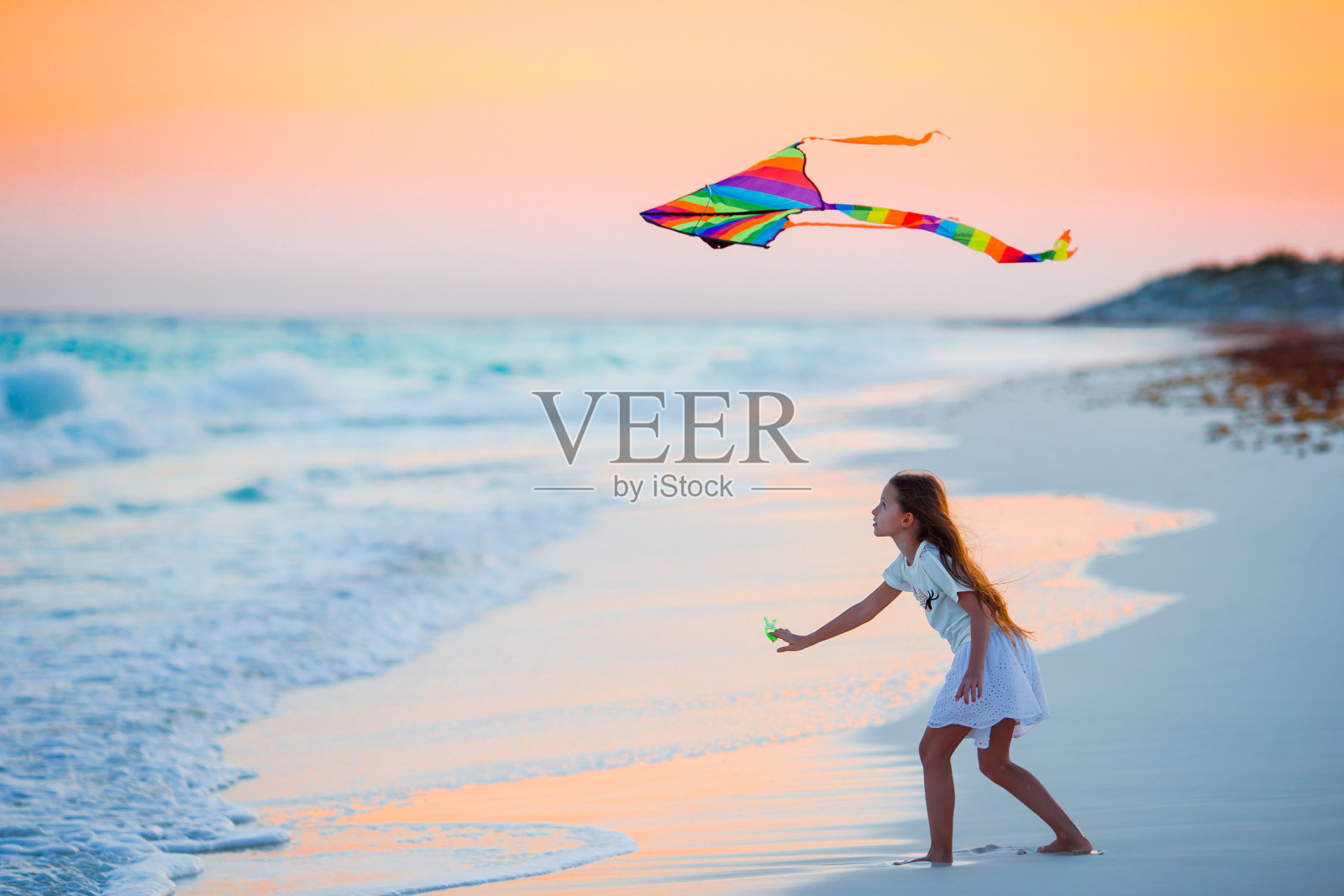 小女孩跑着放风筝在热带海滩上日落。孩子们在海边玩耍。有沙滩玩具的孩子。照片摄影图片