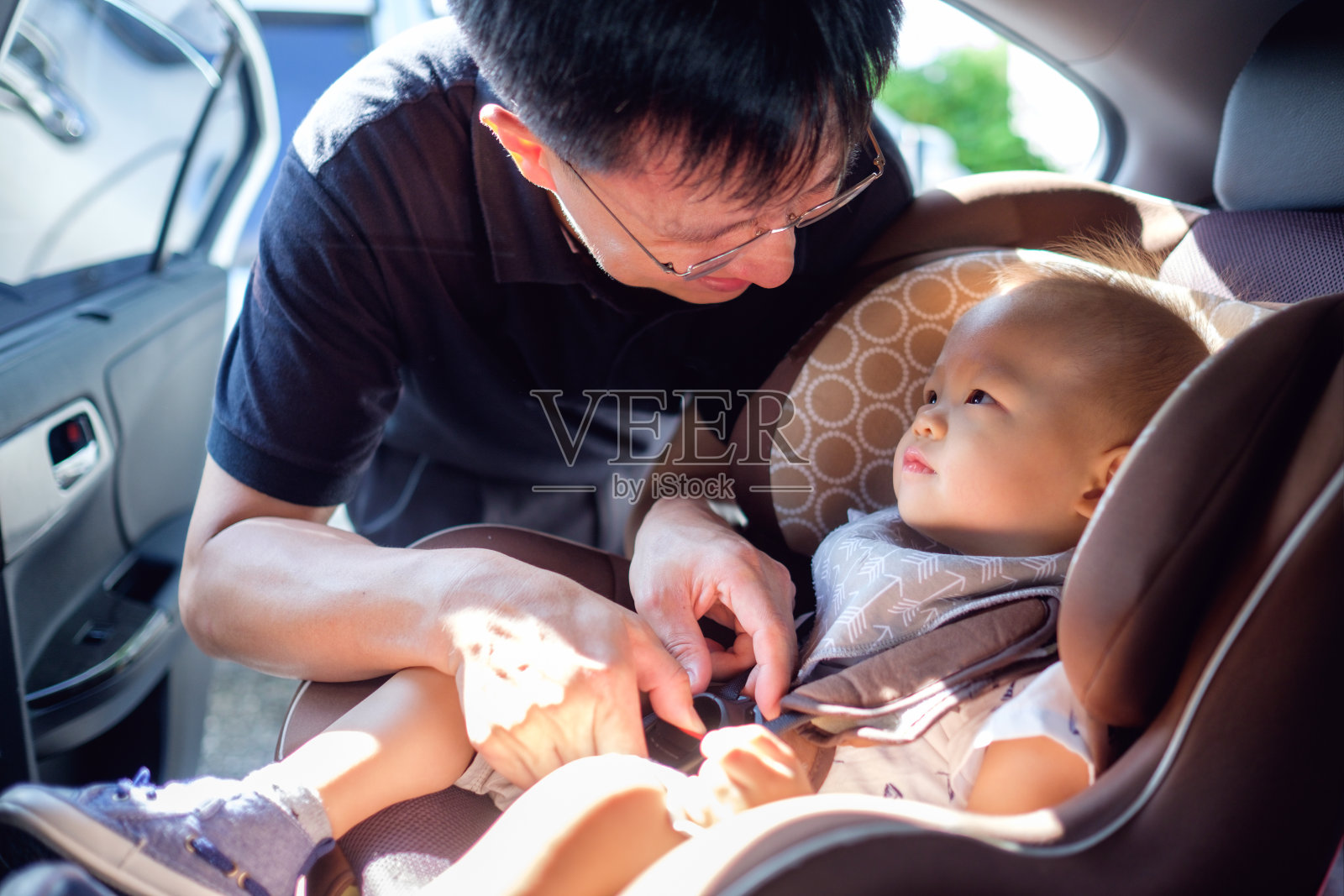 亚洲父亲帮助他可爱的1岁的蹒跚学步的小男孩在汽车上系安全带照片摄影图片