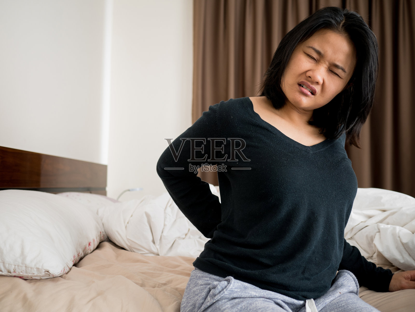 坐在床上忍受背痛的女人照片摄影图片