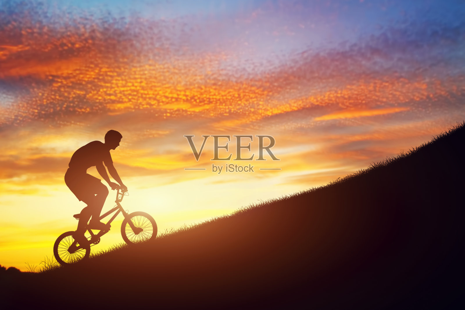 夕阳下，一名男子骑着小轮车上山。力量,挑战。照片摄影图片