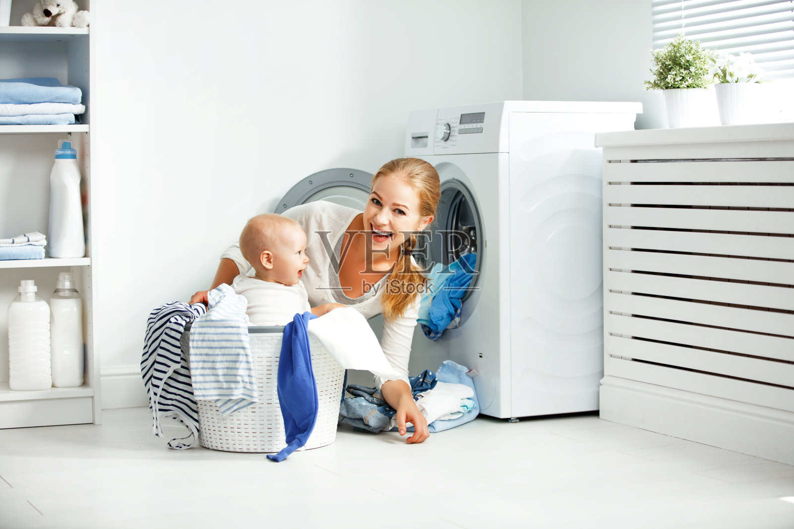 母亲家庭主妇与婴儿从事洗衣折叠衣服到洗衣机照片摄影图片