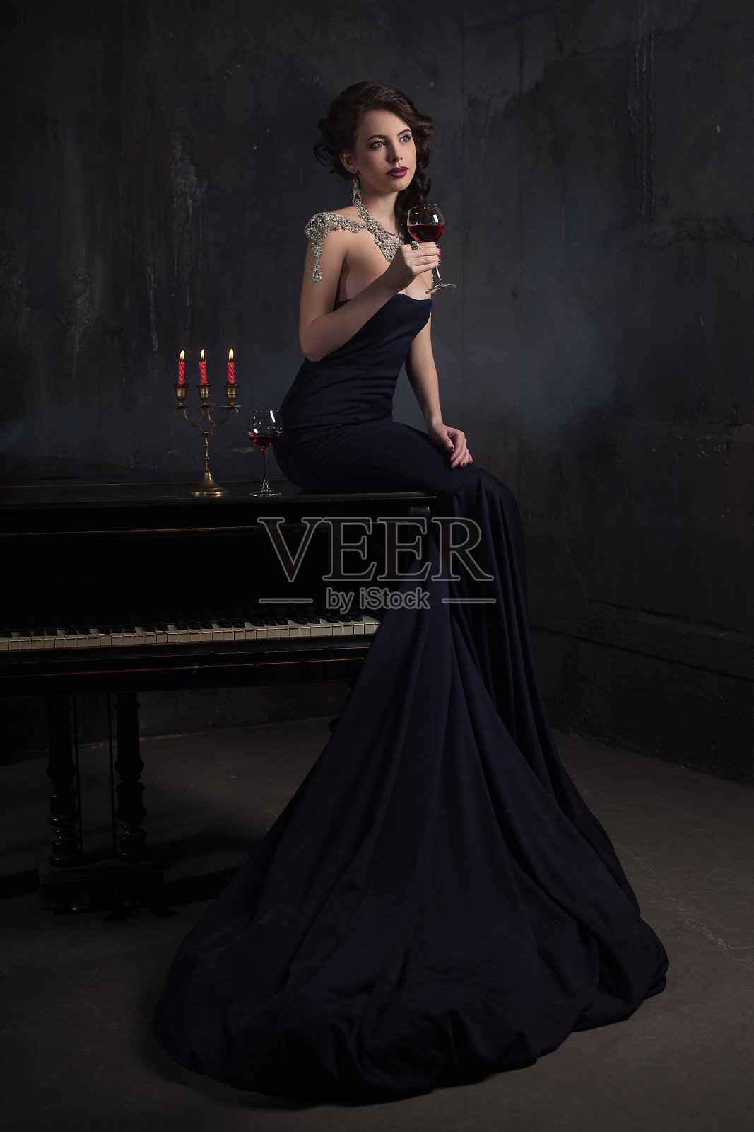 美丽的年轻女子穿着黑色的裙子，旁边有钢琴和烛台蜡烛和葡萄酒，黑暗的城堡气氛戏剧性。波西米亚。照片摄影图片