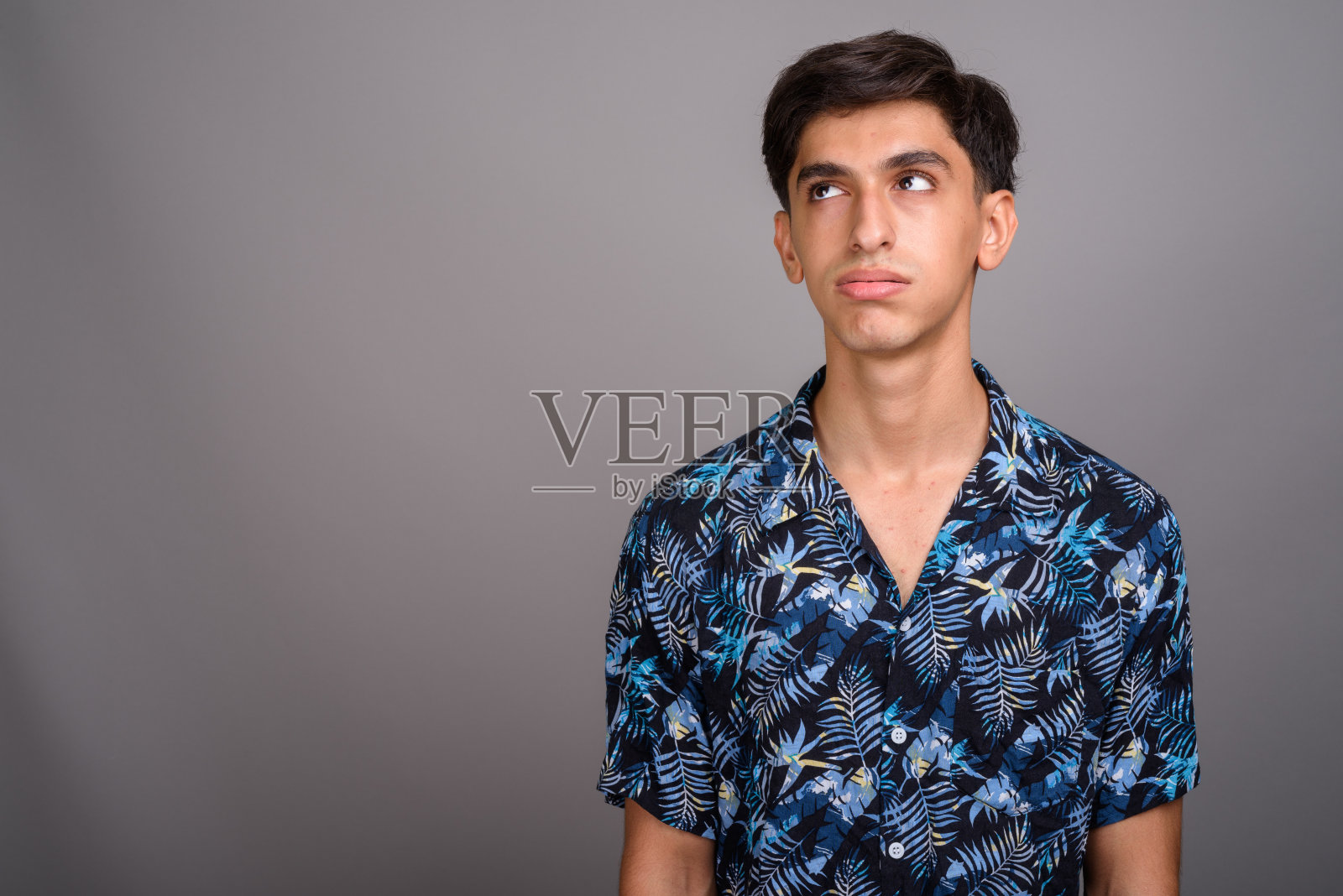 摄影棚里的年轻波斯少年穿着夏威夷衬衫，背景是灰色照片摄影图片