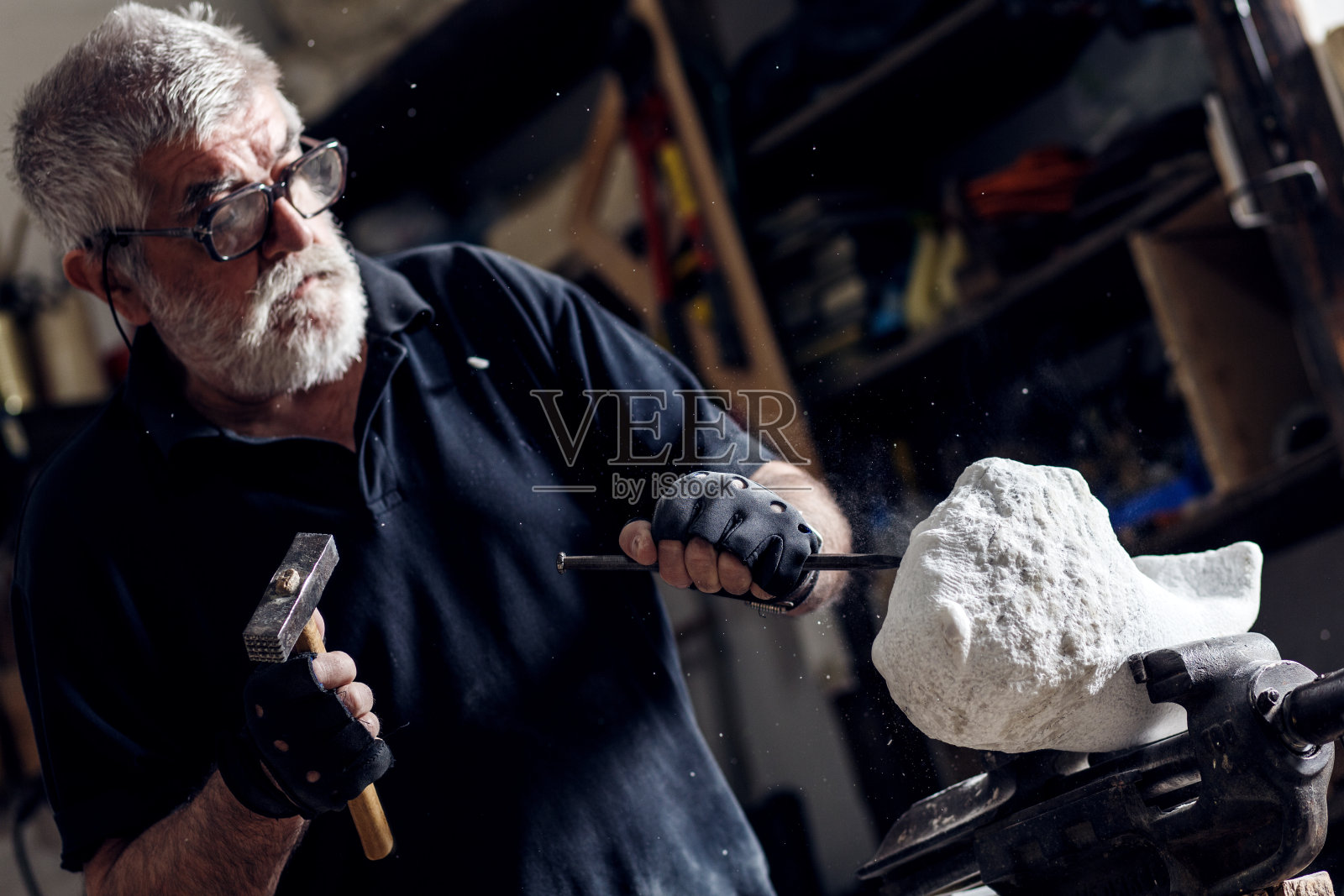 高级雕刻家工作在他的工作室与磨床大理石雕塑。照片摄影图片