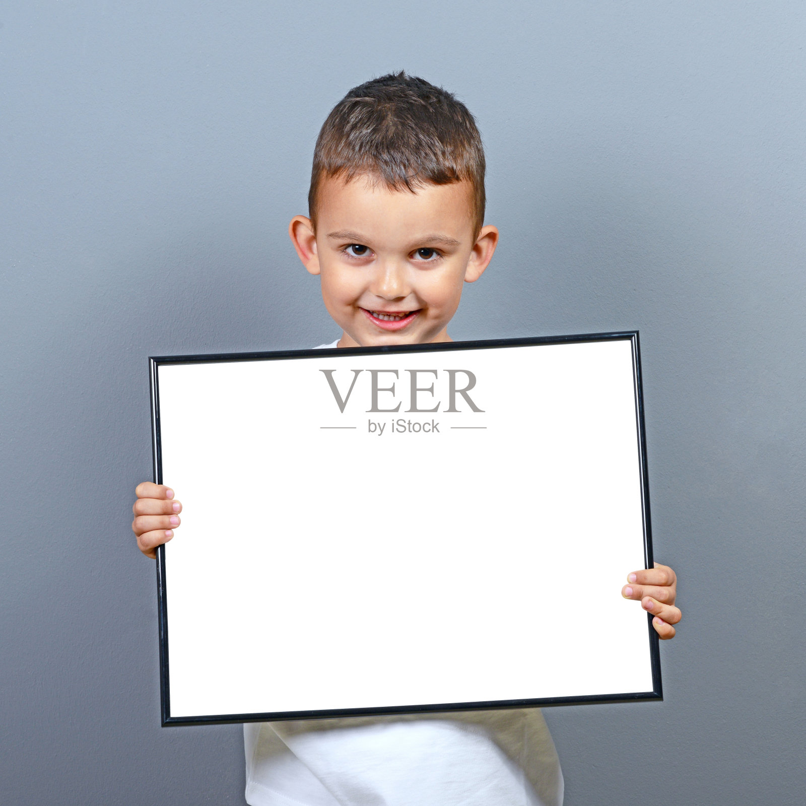 可爱的小男孩拿着空白板，在灰色背景下写一些文字照片摄影图片