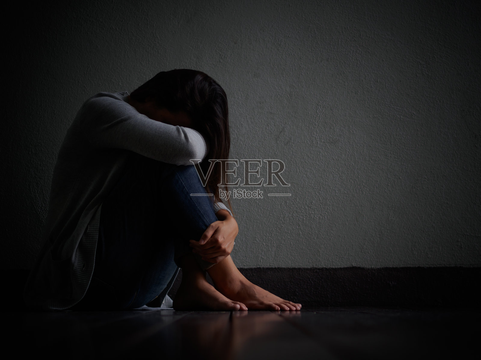 悲伤的女人抱着膝盖哭泣。一个悲伤的女人独自坐在空荡荡的房间里。照片摄影图片