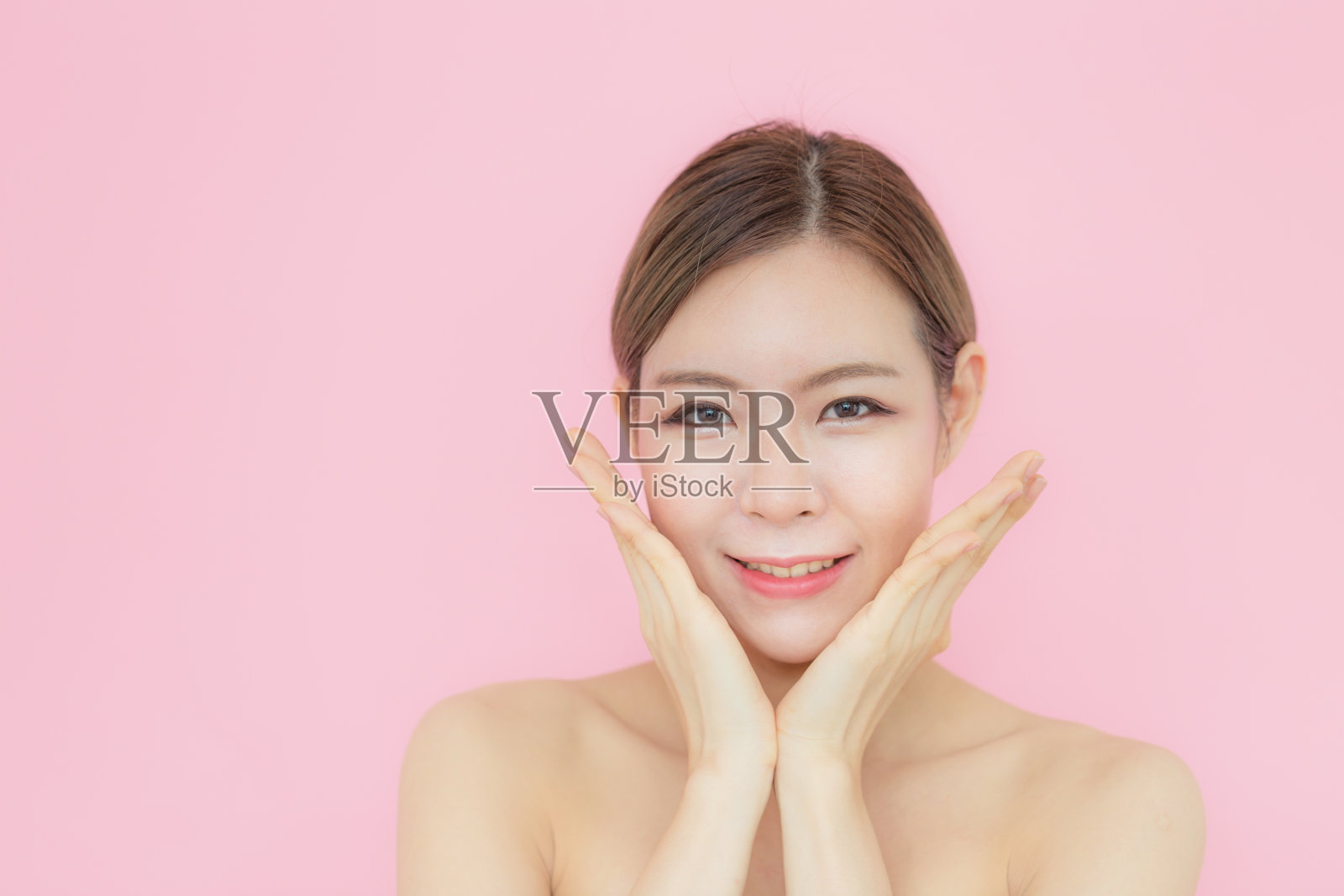 亚洲美丽的女人触摸她的脸像一个v型完美的皮肤与复制空间，孤立在粉红色的背景照片摄影图片