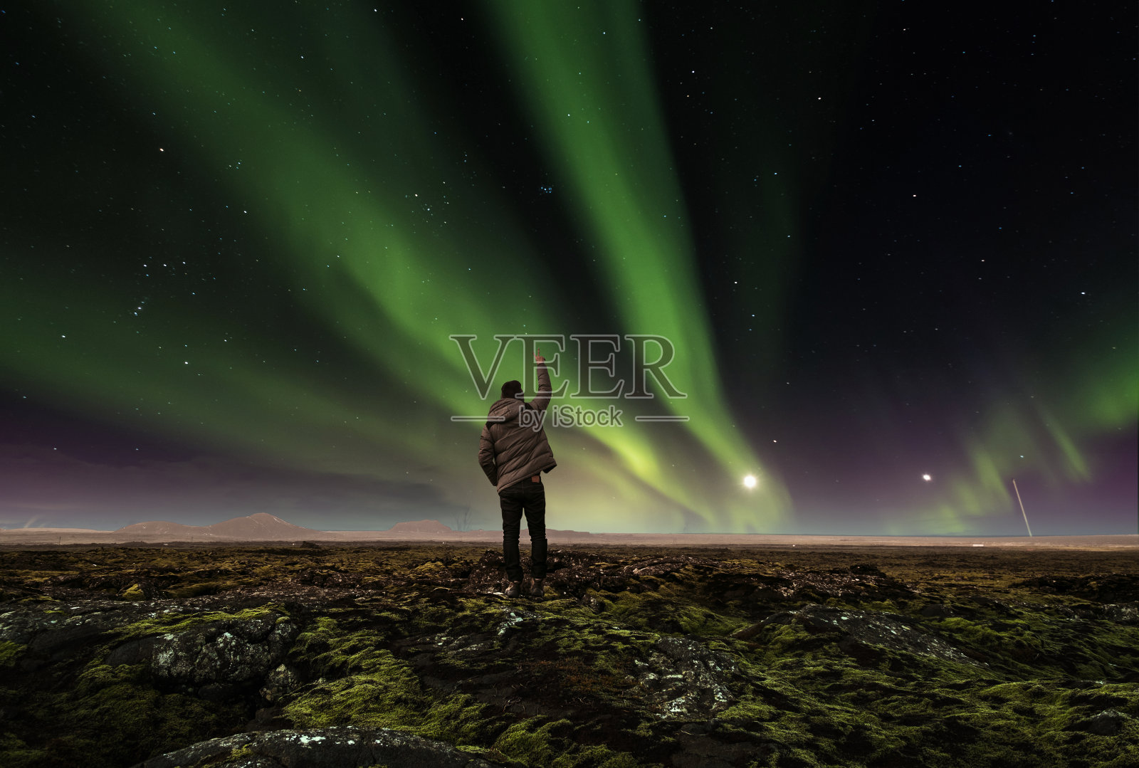 令人惊叹的美丽自然景观北极光，一个男人举起手臂，在冰岛旅行照片摄影图片