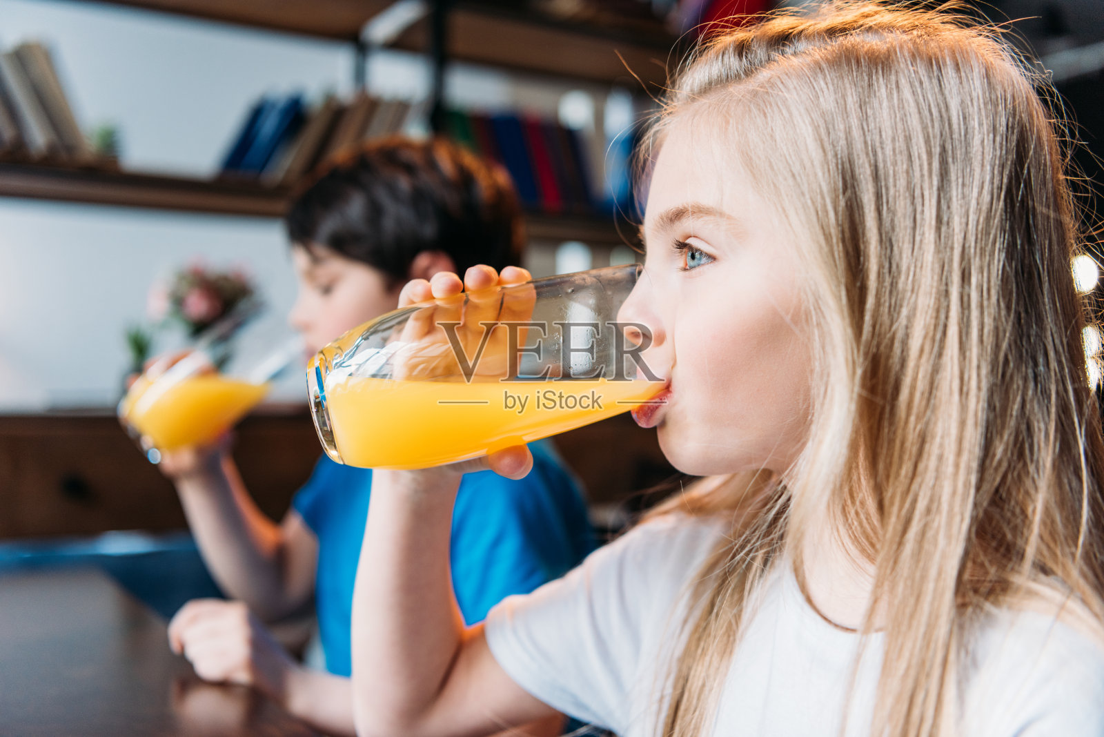 侧面的女孩喝橙汁与男孩附近照片摄影图片