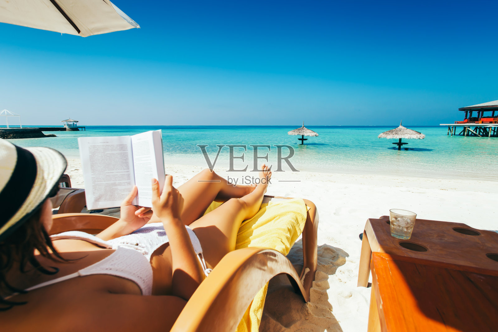 一名女子在热带岛屿的阳伞下躺在日光浴床上看书照片摄影图片