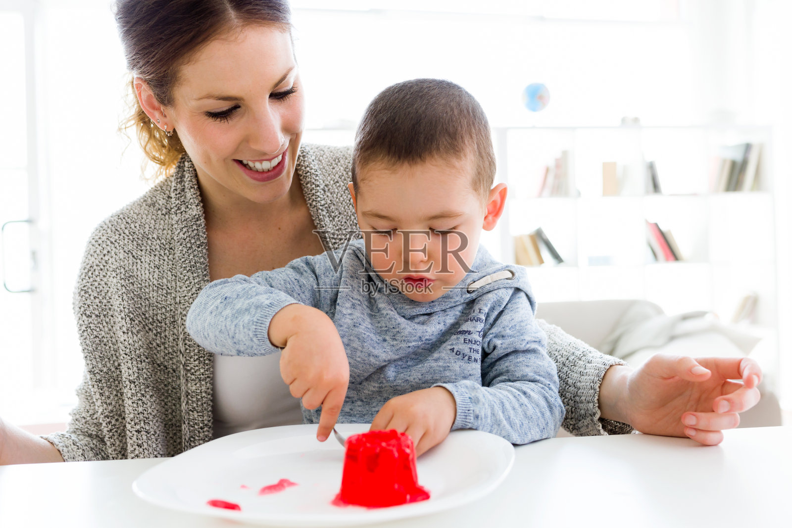 年轻漂亮的妈妈和她的儿子在家里吃草莓果冻。照片摄影图片