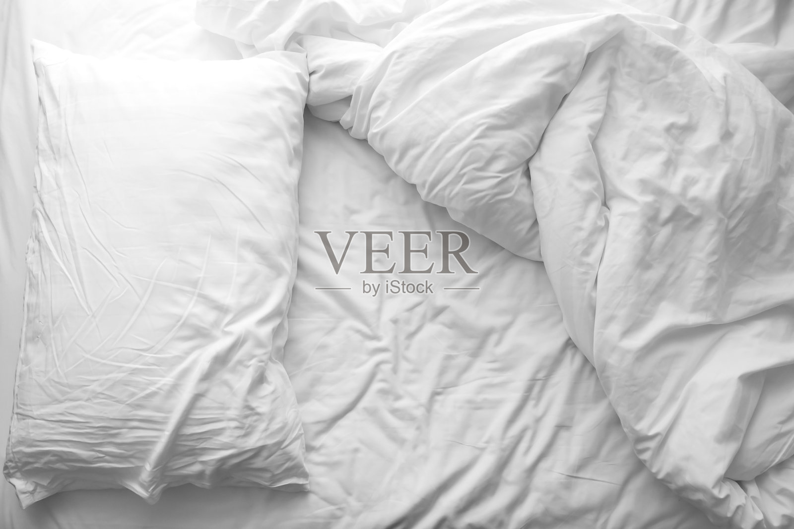 凌乱的床上。床上的白色枕头和毛毯未整理。早晨过后放松的概念。照片摄影图片