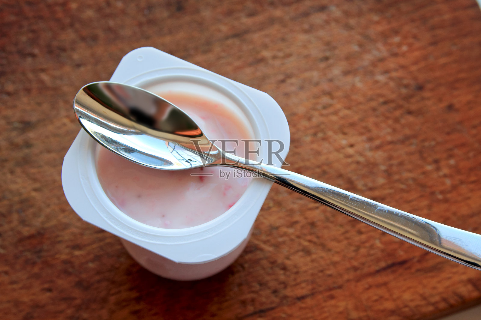 粉红色的酸奶在塑料杯和勺子的木制背景。照片摄影图片