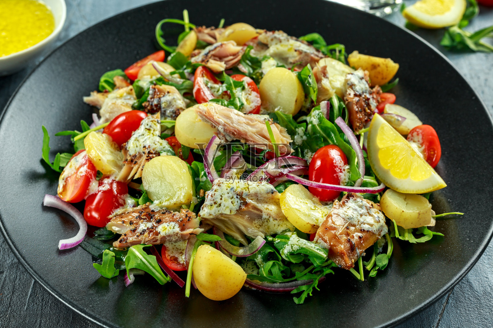 烟熏鲭鱼沙拉配热煮的新土豆，樱桃番茄，红洋葱和Ruccola在黑色的盘子。照片摄影图片