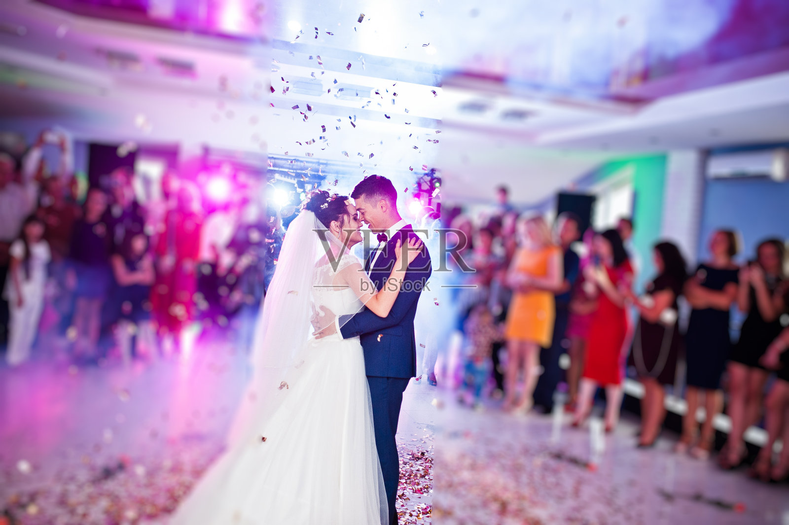这是新人在婚礼上以五彩纸屑和彩灯为背景的感人的第一支舞。照片摄影图片