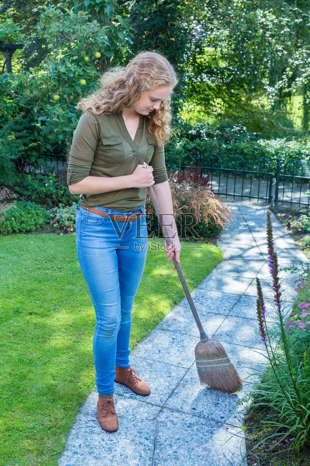 年轻的荷兰女子用柳条扫帚清扫花园小径照片摄影图片