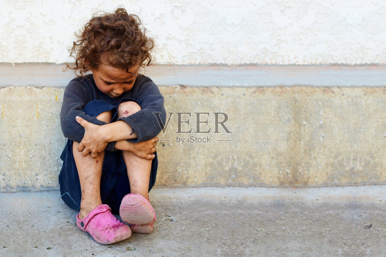 可怜而悲伤的小女孩靠在水泥墙上照片摄影图片
