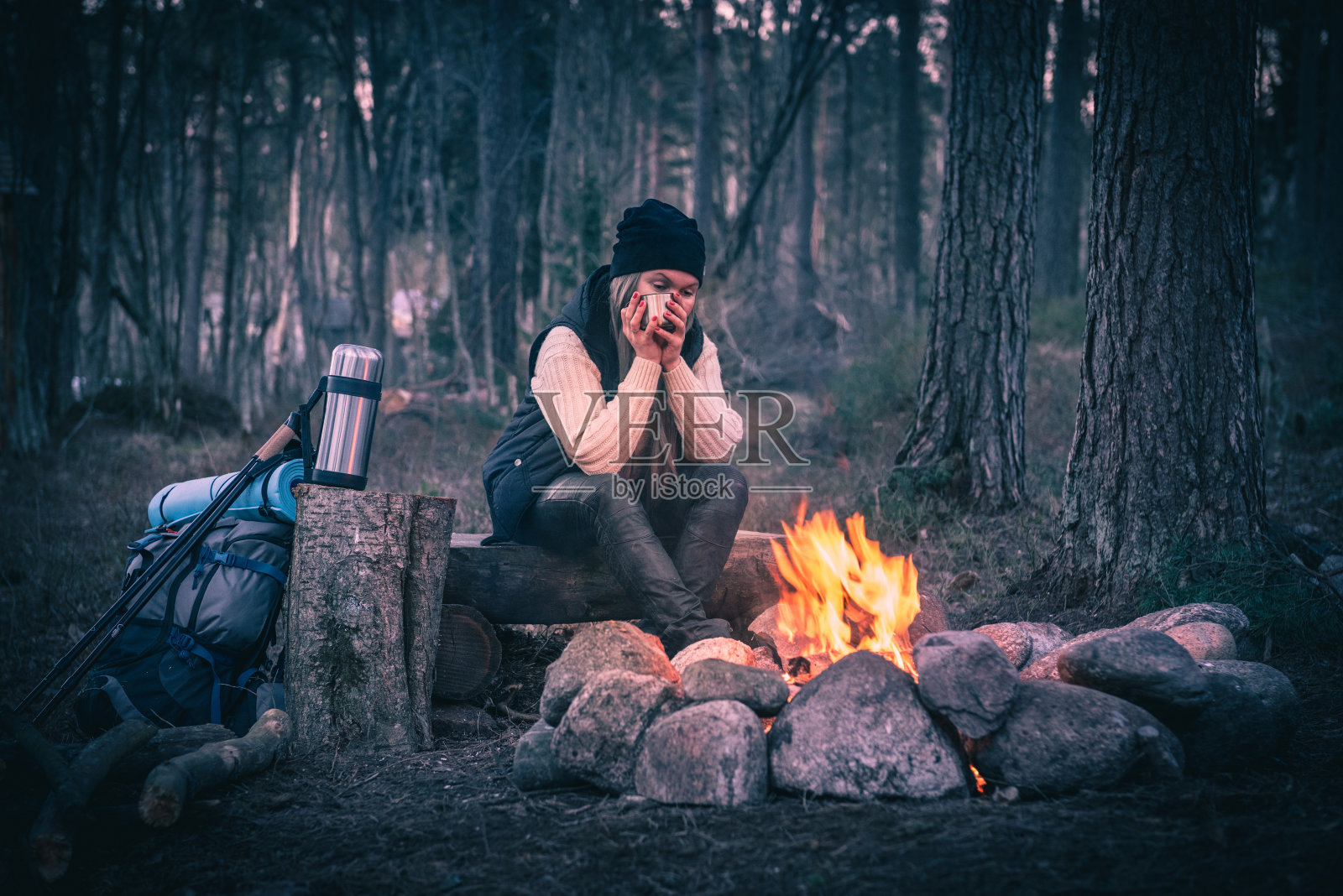 一个女人在篝火旁休息，喝着热饮照片摄影图片