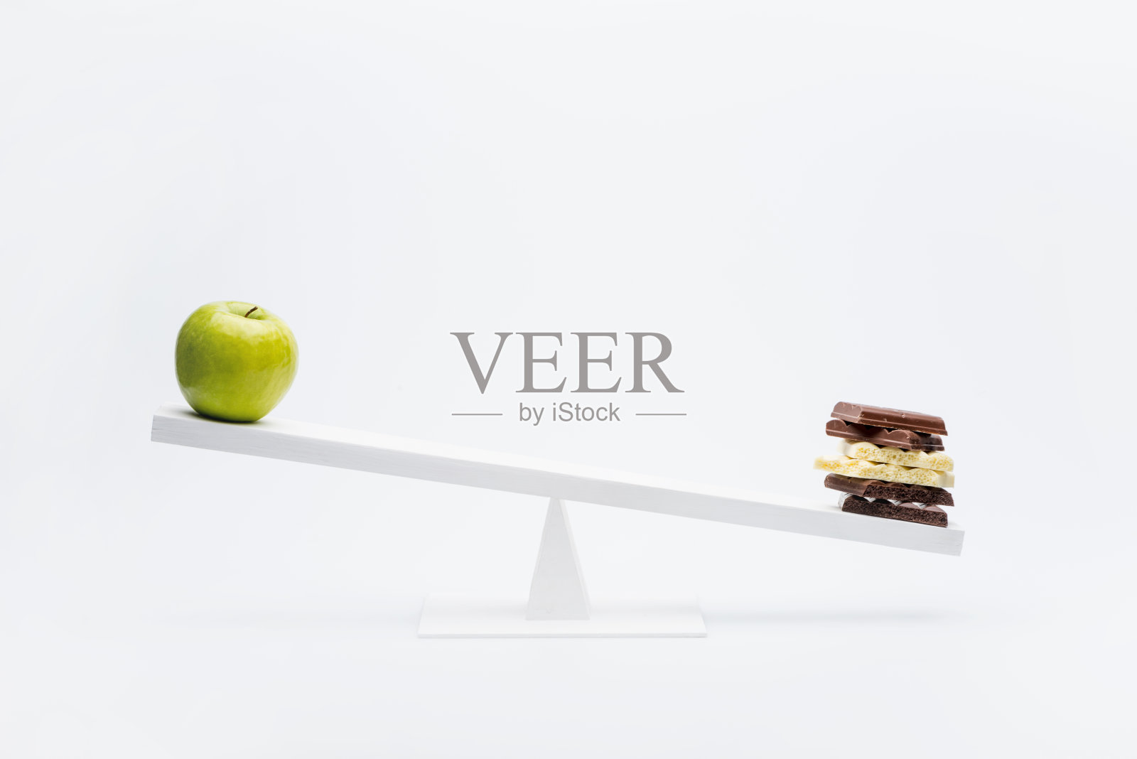 苹果和巧克力在跷跷板上平衡的特写，健康的生活理念照片摄影图片