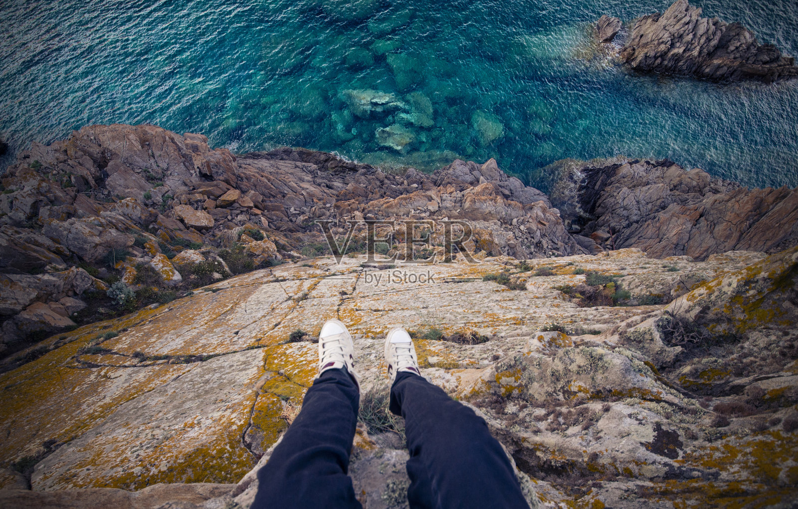 一个男人站在意大利海岸的悬崖上，下面是地中海。波尔图切尔沃-翡翠海岸，撒丁岛-意大利照片摄影图片