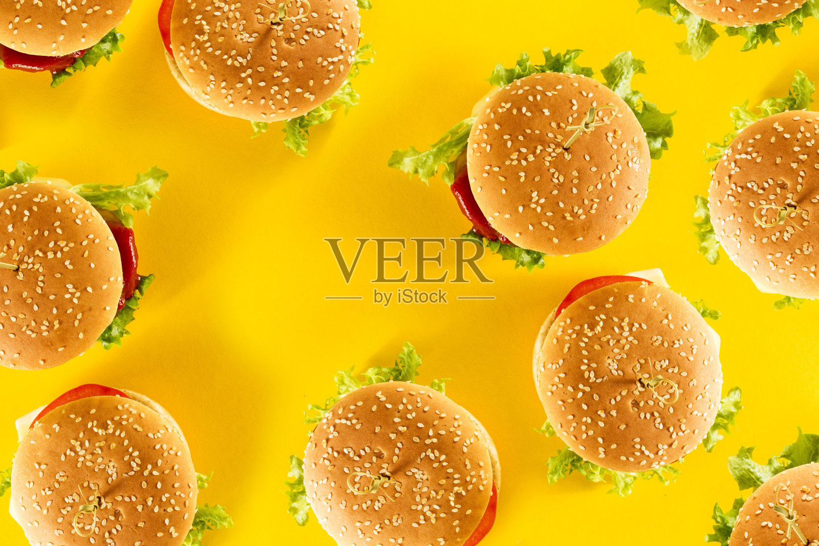 许多美味的新鲜的不健康的汉堡包与蕃茄酱和蔬菜在黄色明亮的背景。顶部视图与复制空间。照片摄影图片
