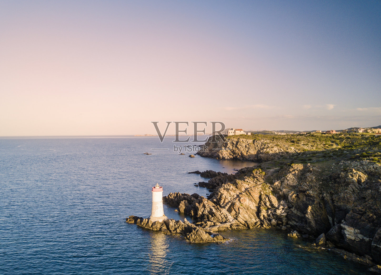 日落时意大利海岸的鸟瞰图，地中海上有一座灯塔。波尔图切尔沃-翡翠海岸，撒丁岛-意大利照片摄影图片
