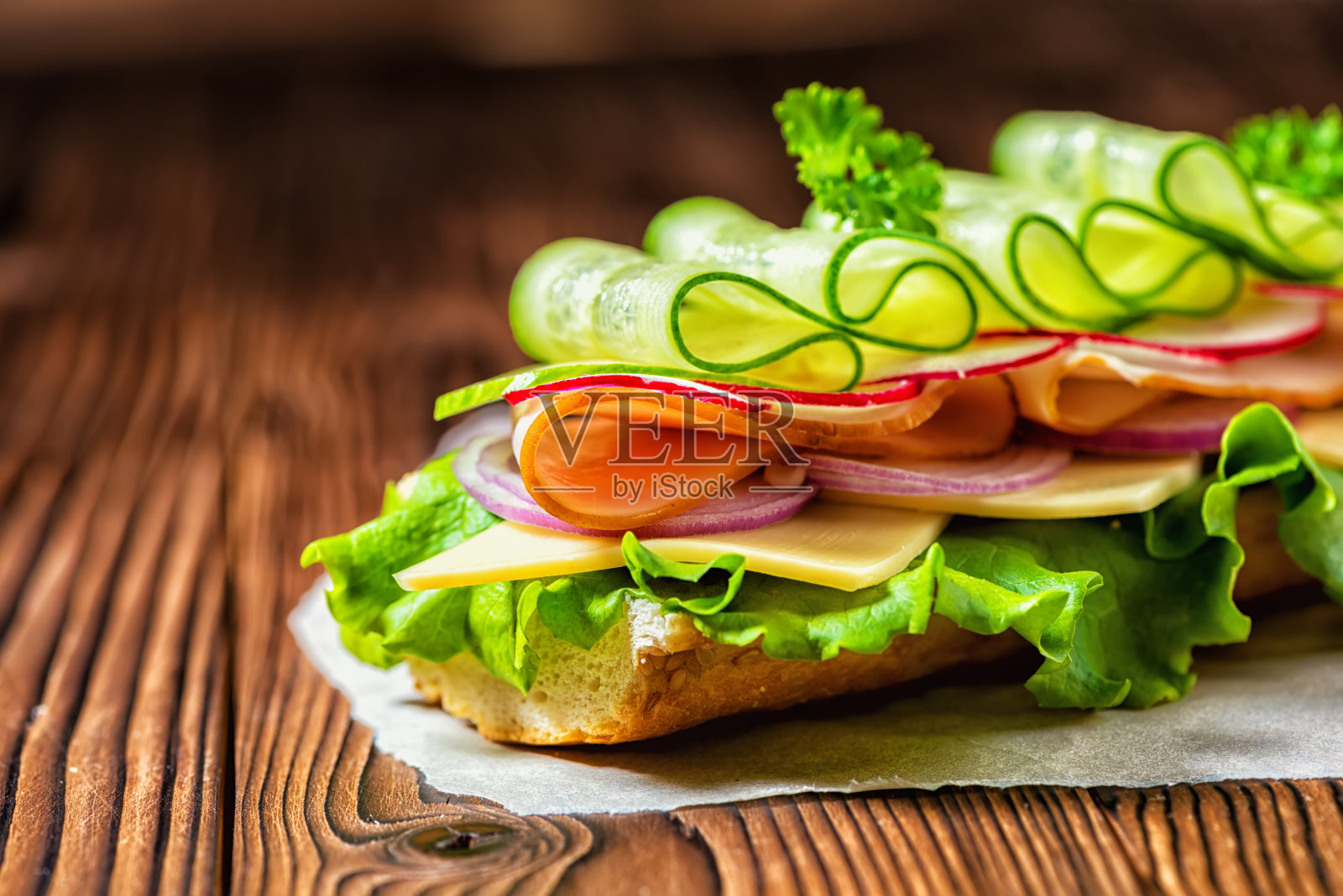 特写的三明治与火腿，奶酪，培根，萝卜，生菜，黄瓜和洋葱在纸上，木制的背景照片摄影图片