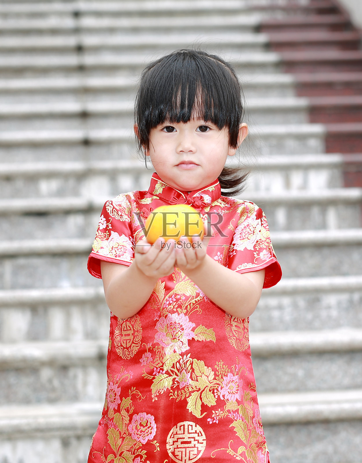 可爱的亚洲小女孩穿着传统的中国服装，拿着神圣的橙色。照片摄影图片