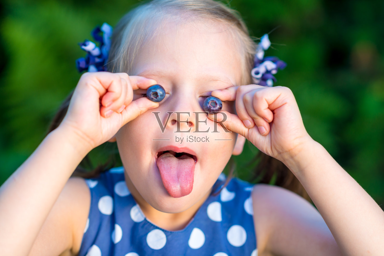 微笑的女孩把蓝莓举在面前，露出她的舌头照片摄影图片