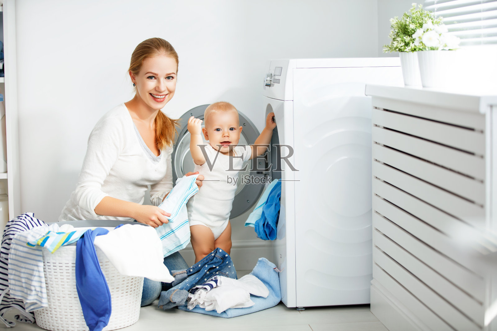 母亲家庭主妇与婴儿从事洗衣折叠衣服到洗衣机照片摄影图片
