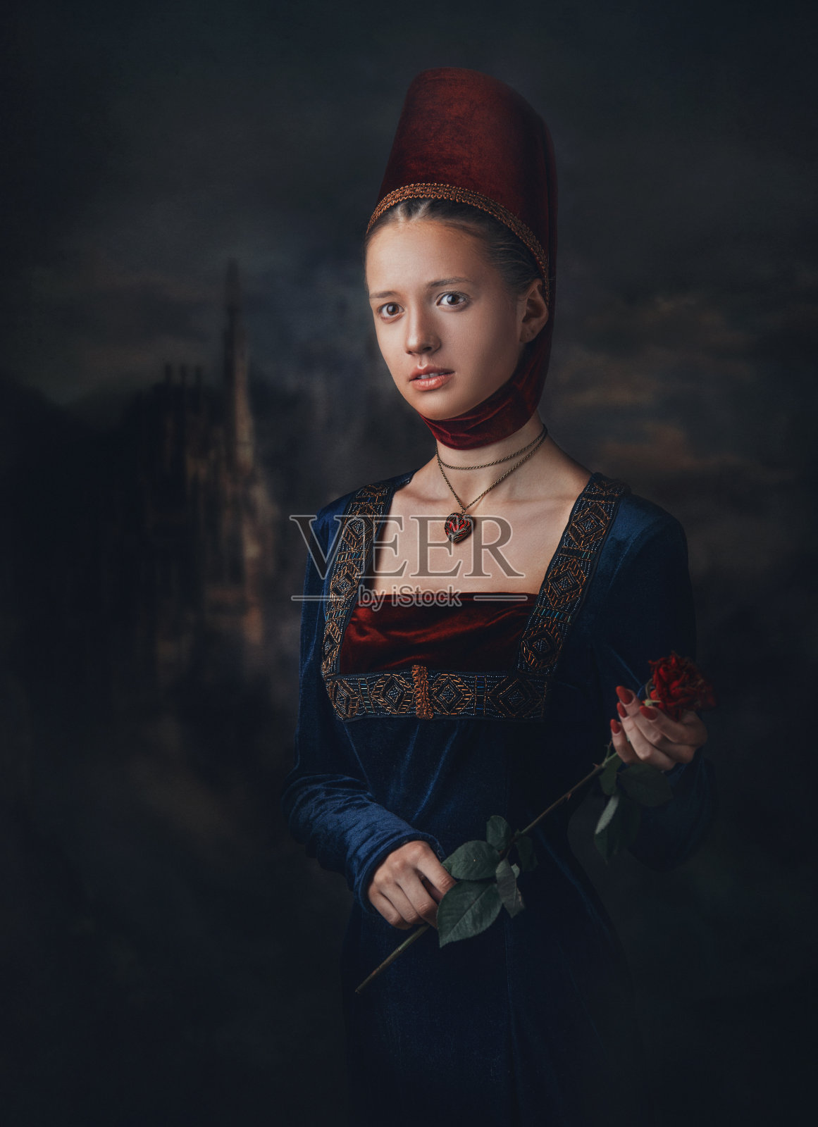 一个美丽的中世纪女孩的肖像穿着和头饰。心形的奖章。手里捧着一朵红玫瑰。照片摄影图片