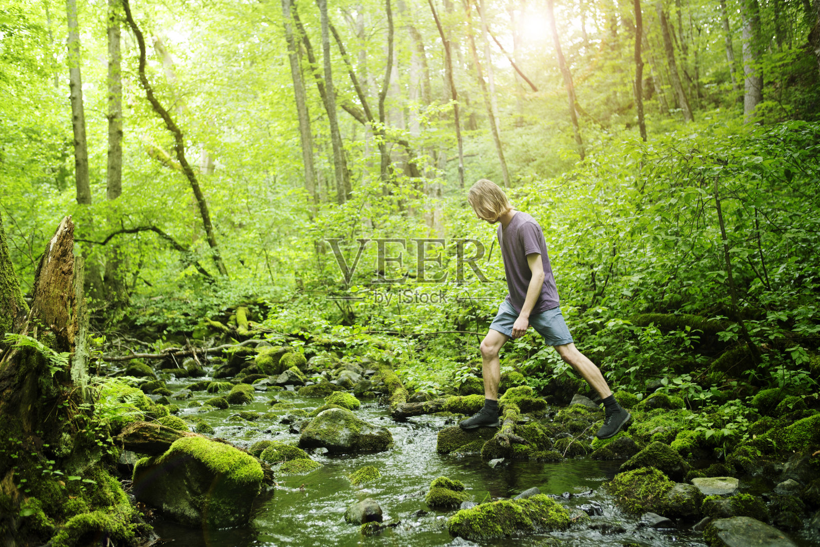 一个年轻人正在绿色的森林里穿过一条小溪照片摄影图片