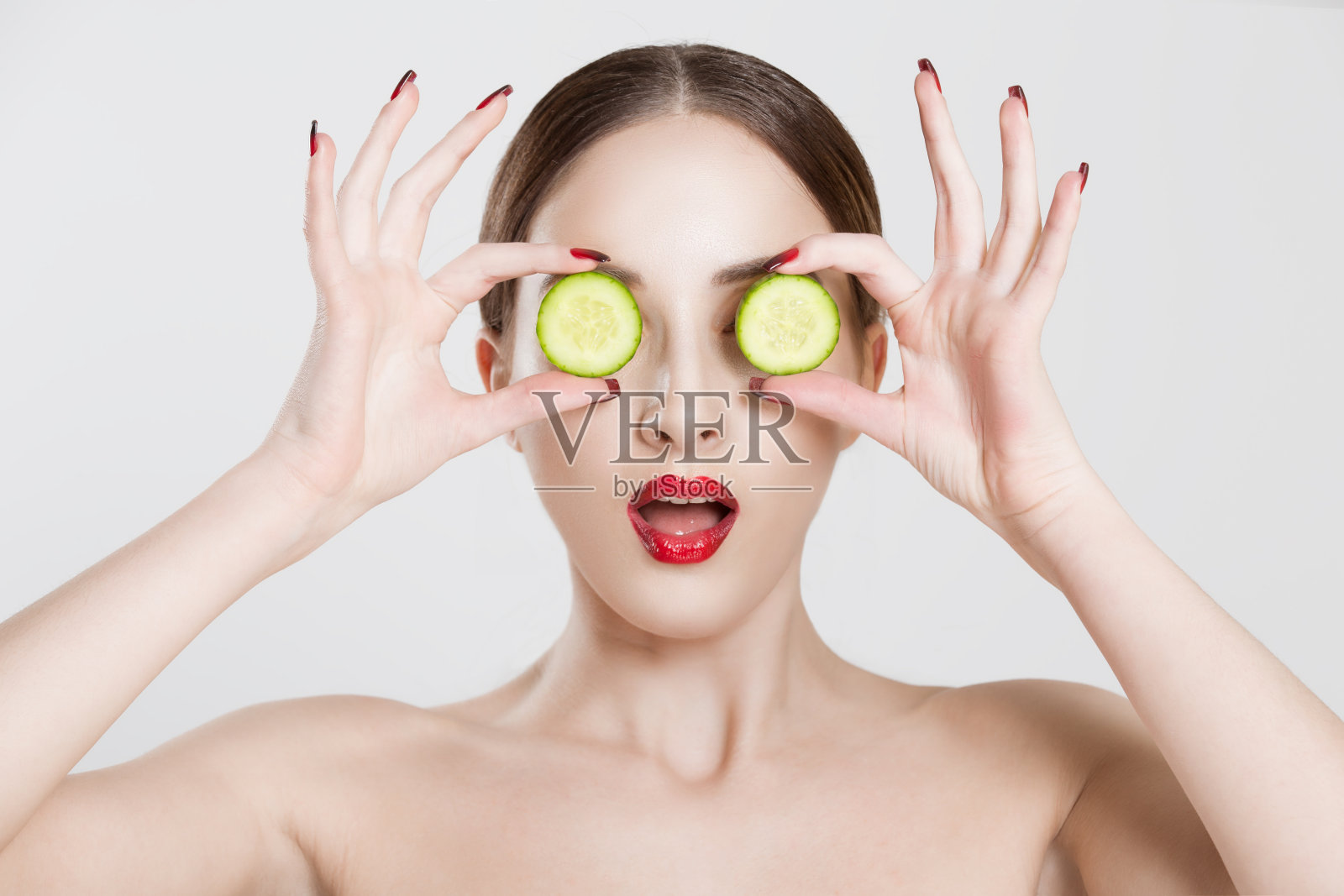女人惊讶地用黄瓜把眼睛孤立在白色背景墙上照片摄影图片