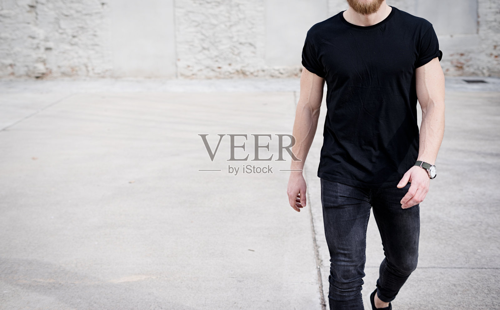 年轻的肌肉男穿着黑色t恤和牛仔裤走在市区。模糊的背景。Hotizontal模型。照片摄影图片