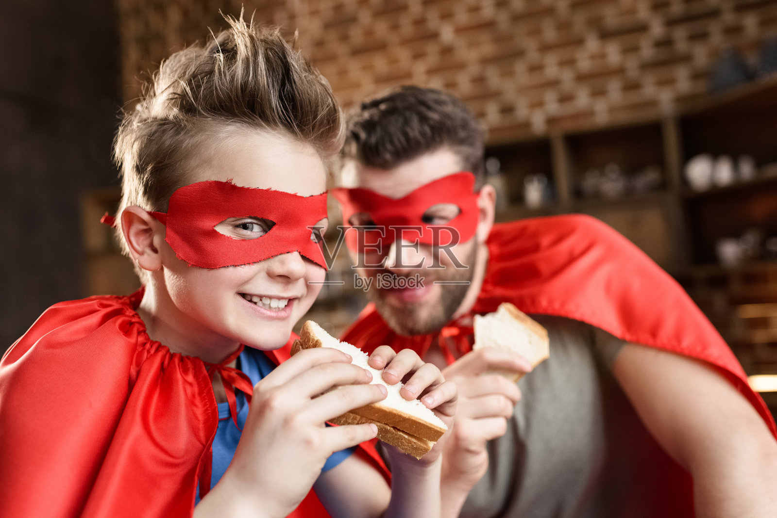 父子俩穿着红色超级英雄服装在家吃三明治照片摄影图片
