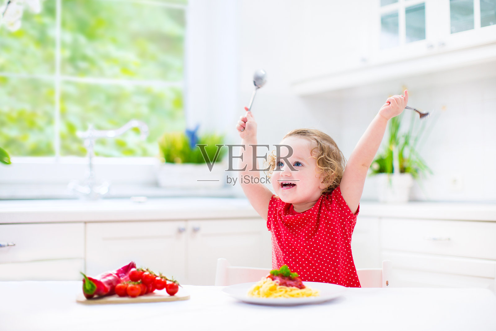 可爱的笑着蹒跚学步的女孩用叉子和勺子吃意大利面照片摄影图片