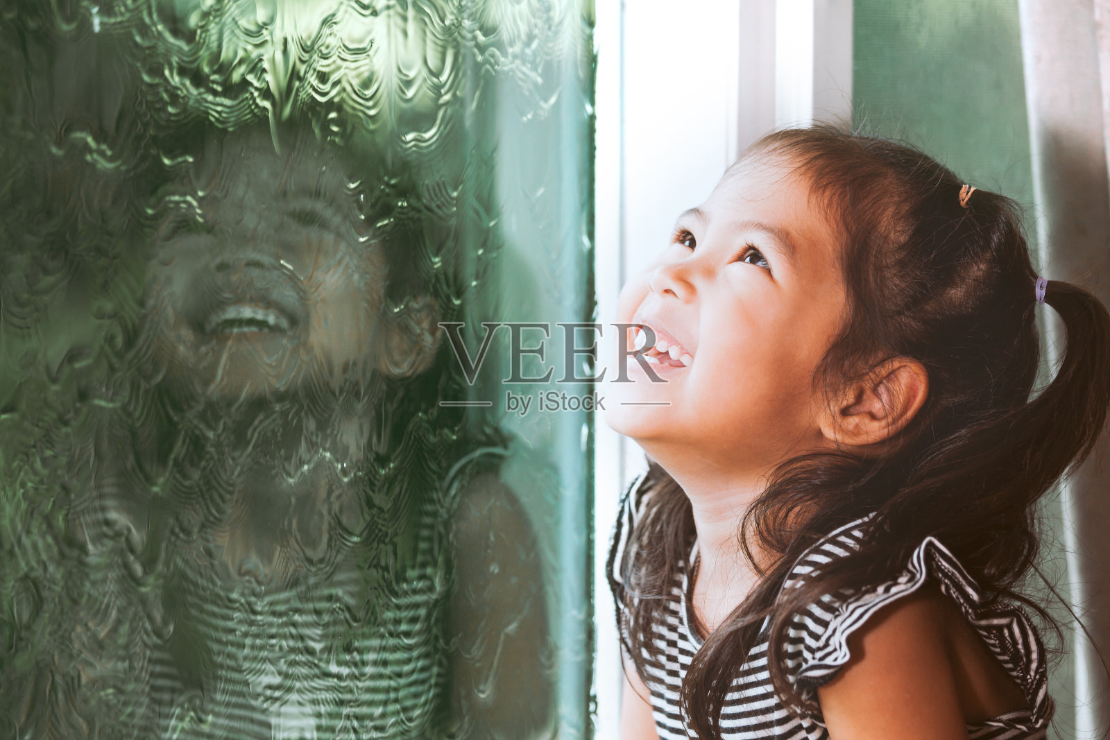 快乐的亚洲小女孩望着窗外在雨天照片摄影图片