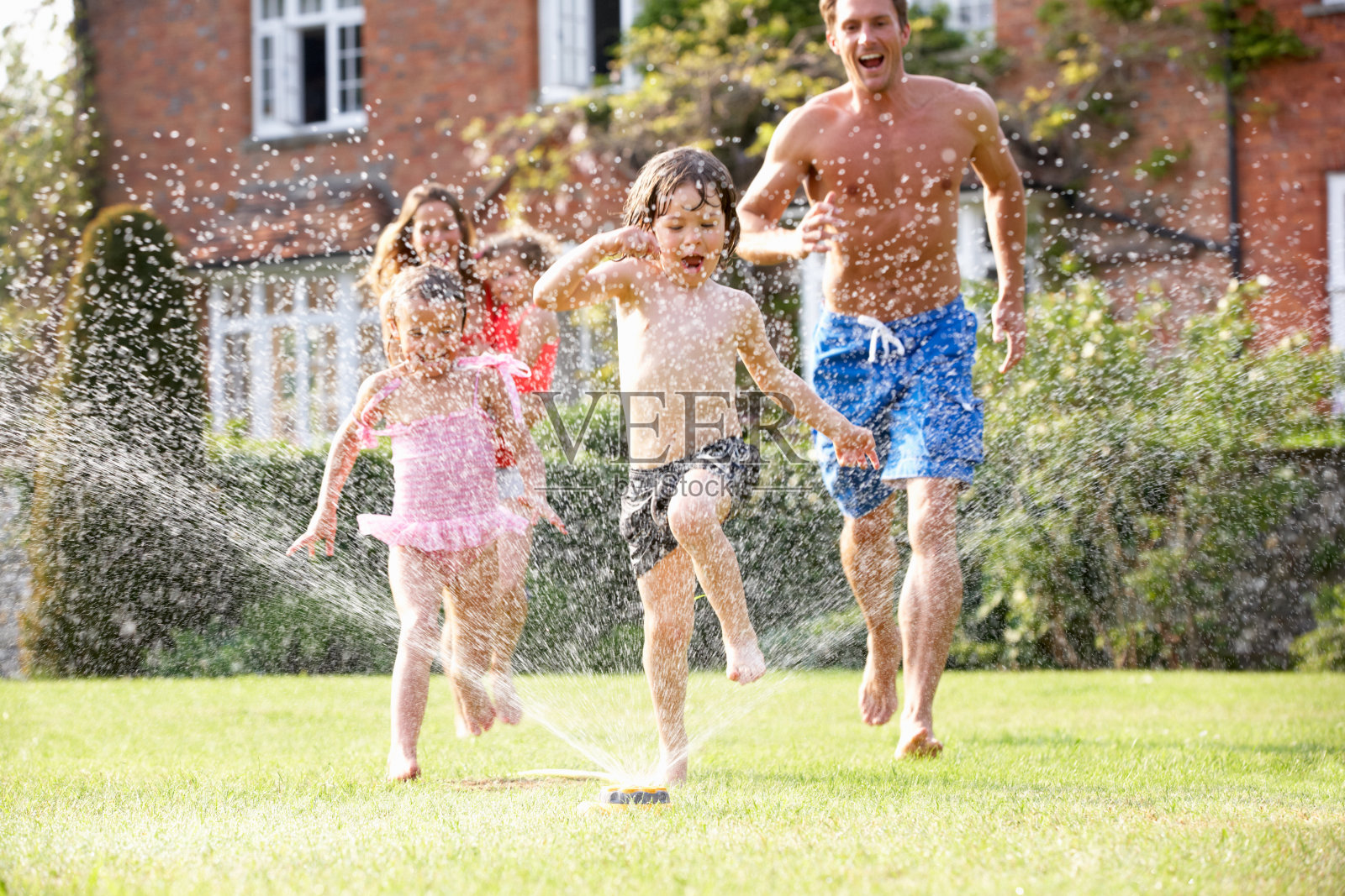 一个快乐的家庭跑过洒水器照片摄影图片