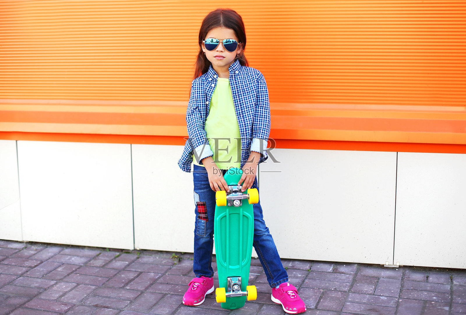 时髦的小女孩与滑板在橙色的背景照片摄影图片