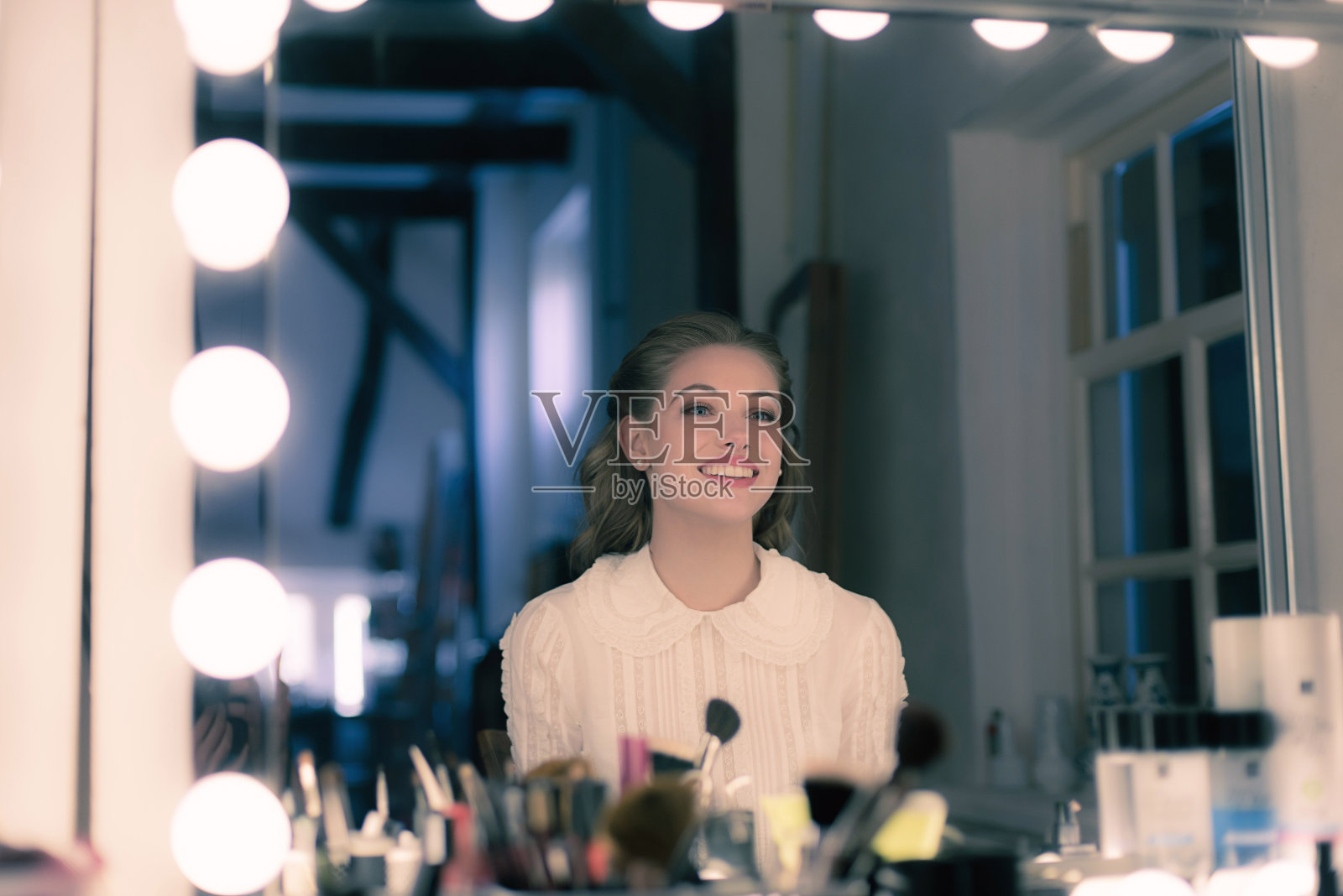 微笑的漂亮年轻女人复古四十年代风格看着剧院的镜子。照片摄影图片